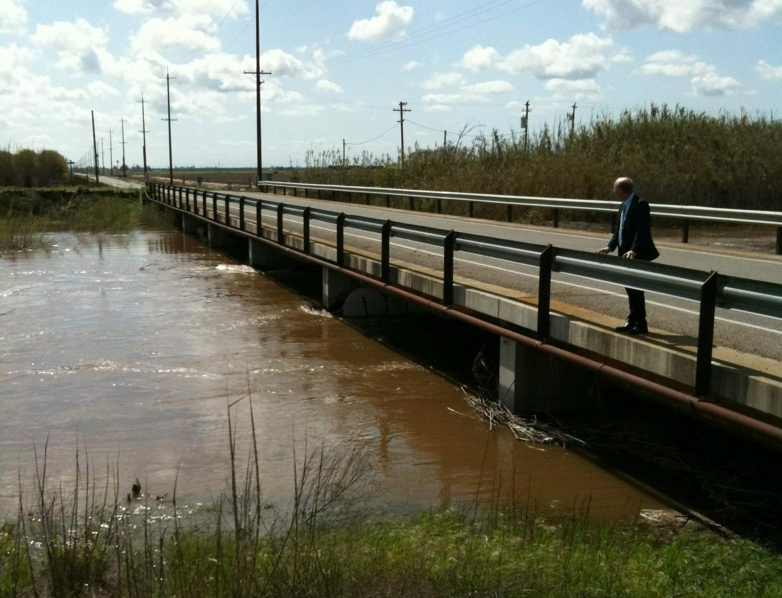 Supervisor David Rogers overlooking a high flowing waterway from a bridge.