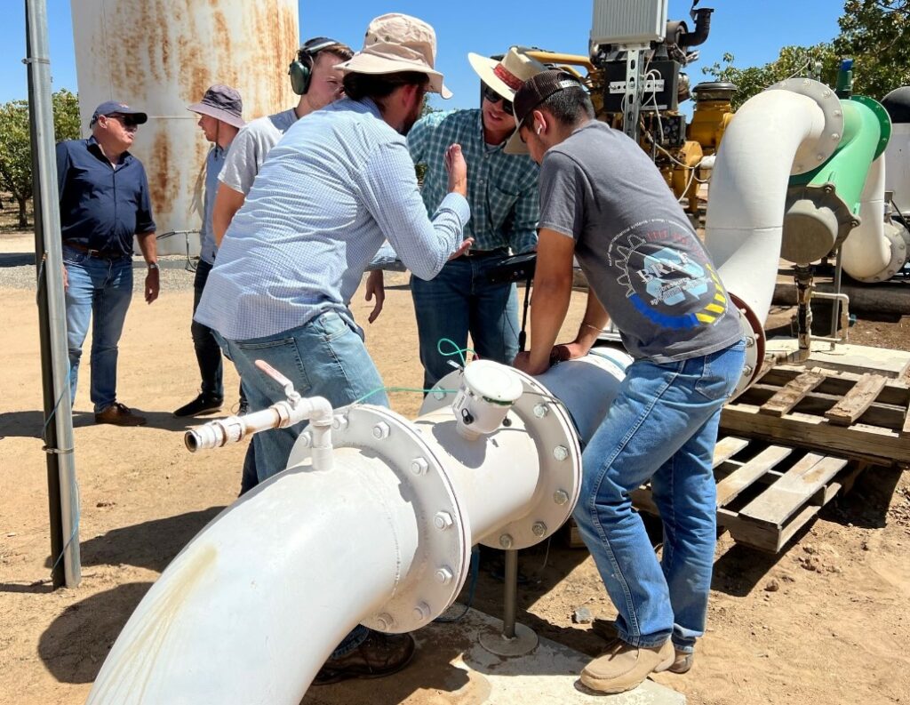 Field staff having a discussion and examining a flowmeter in the field.